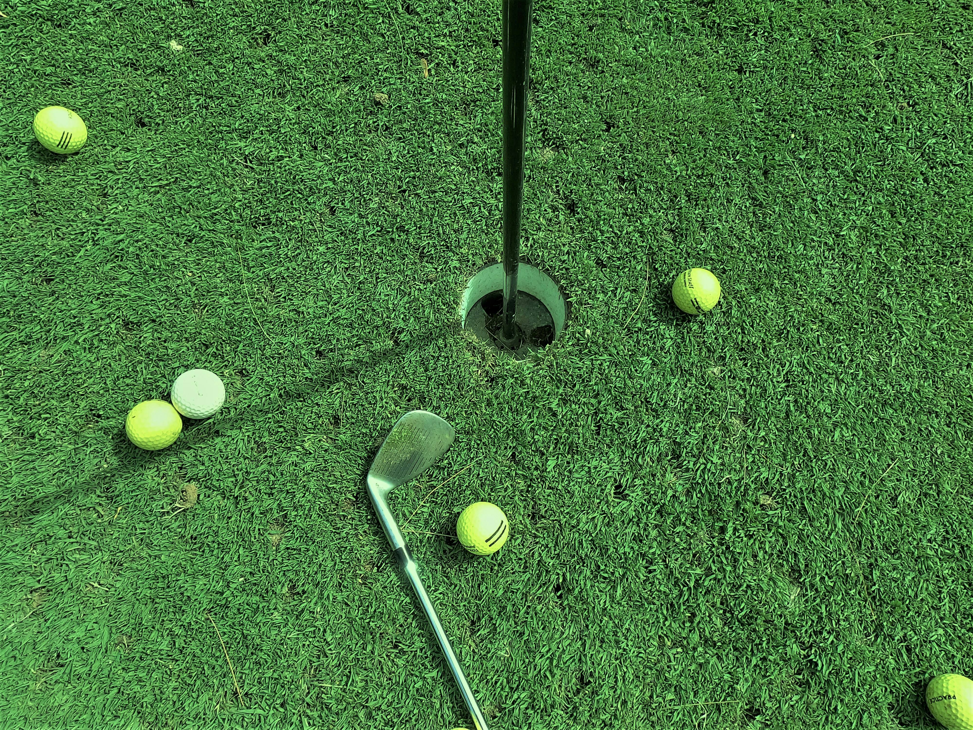 Golf balls scattered around a hole and flag on green turf during a putting challenge